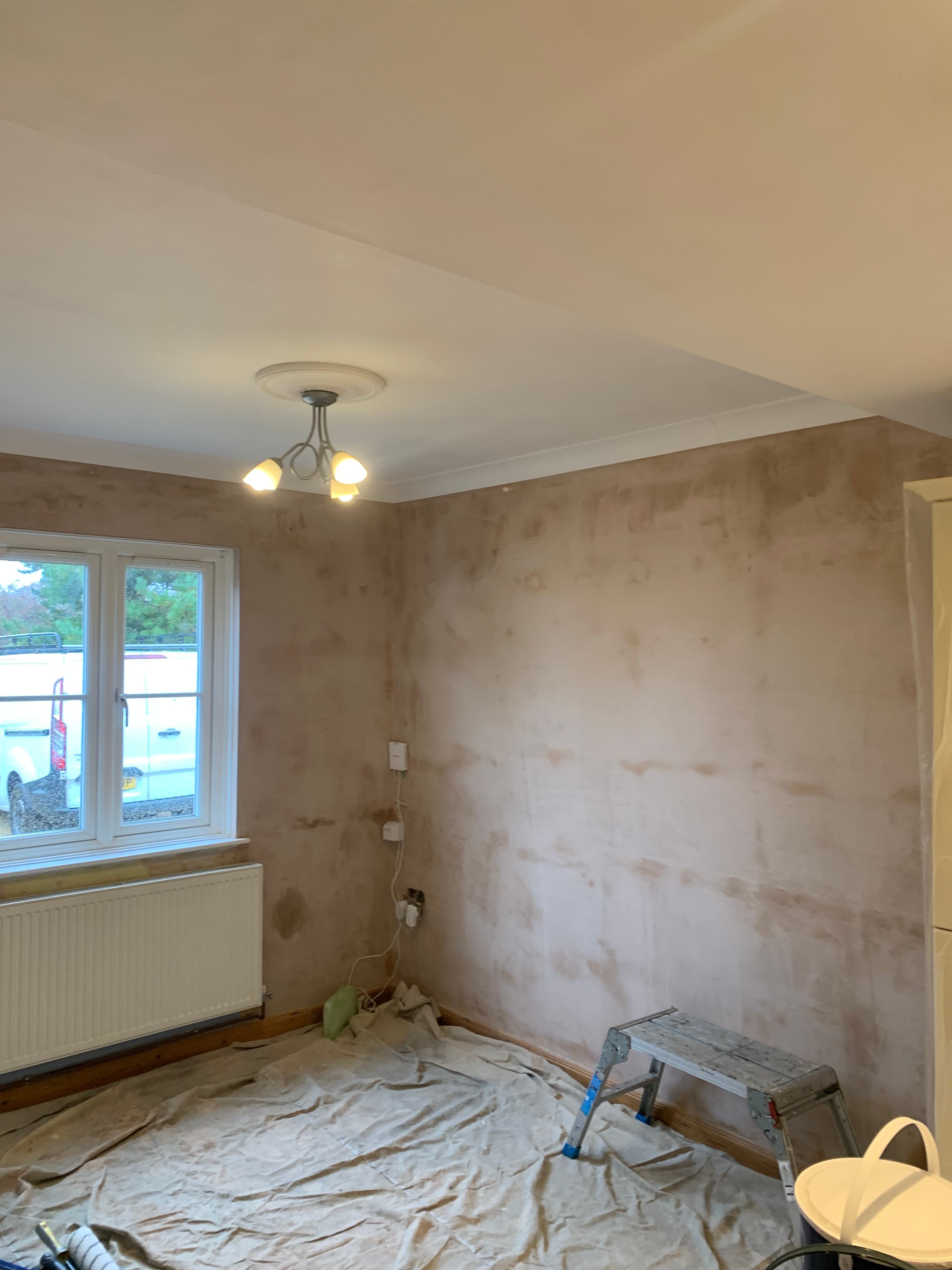 Room undergoing renovation with freshly plastered walls, floor drop cloths, and a step ladder.